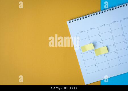 Calendar page with yellow adhesive notes. On top of blue and yellow surface. Copy space. Stock Photo