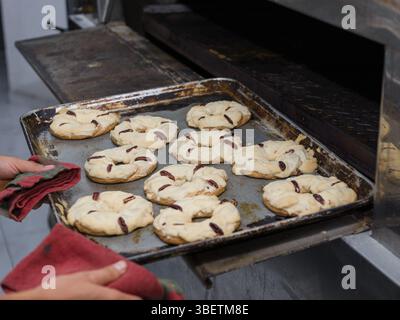 A baking sheet of freshly baked ring-shaped cookies, topped with pecans, is carefully removed from an oven. Stock Photo