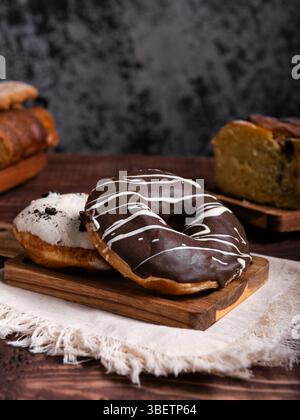 Two delicious donuts, one chocolate and the other cookies and cream on a wooden board. Blurred background with baked goods. Stock Photo