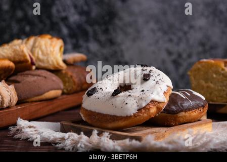 Two delicious donuts, one chocolate and the other cookies and cream on a wooden board. Blurred background with baked goods. Stock Photo