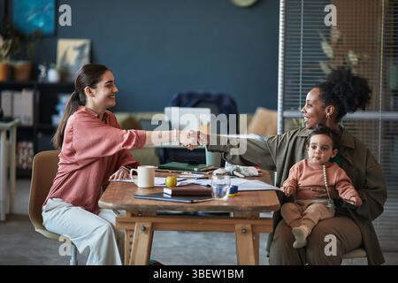Two women engaging in business consultation while one holds baby in lap. Showing collaborative work environment and friendly interaction in profession Stock Photo