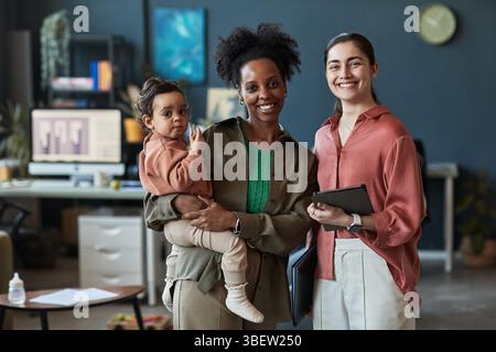 Portrait of smiling multigenerational family standing in modern office environment, holding a baby, while sharing moment of joy and bonding captured i Stock Photo