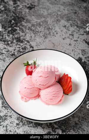 Scoops of pink strawberry ice cream, served with fresh strawberries on a white plate. Stock Photo