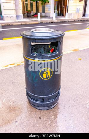 Trash bin with garbage inside in city street. Black recycle bin on the road. Stock Photo