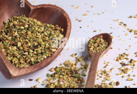 Crushed pistachio nuts in wooden bowl and heart-shaped spoon for cooking. Environmentally friendly product and health. Stock Photo