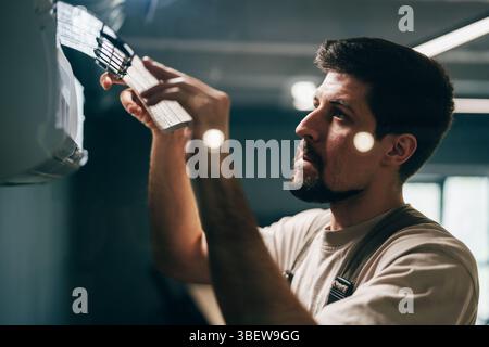 Man performs maintenance on air conditioning unit inside modern building during daylight Stock Photo