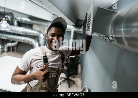 Skilled worker performs maintenance on ventilation system in modern office space during daylight hours Stock Photo