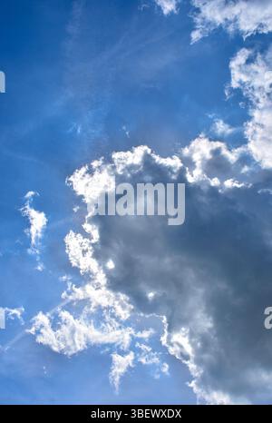 Fluffy clouds with sunlight shining from behind against a vibrant blue sky. Perfect for background or nature themes. Stock Photo