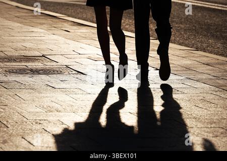 Silhouettes and shadows of couple walking down the street. Female legs in shoes on high heels, concept of relationships, city life, dramatic stories Stock Photo