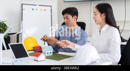 Sustainability and Engineering. Two engineers discussing eco-friendly design solutions with models and tools. Stock Photo