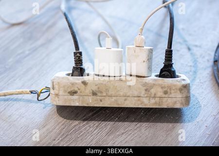 A power strip that is dirty and has three different plugs inserted into it, revealing some worn electrical connections and usage Stock Photo