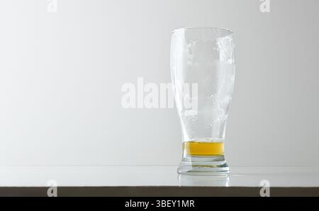 Almost empty beer glass, dirty with foam, reflected on white table and white isolated background. Front view. Stock Photo
