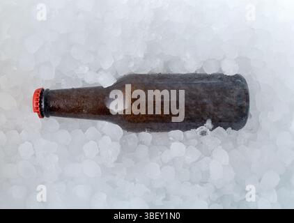 Background with a brown bottle filled with beer half buried in a pile of ice cubes. Top view. Stock Photo