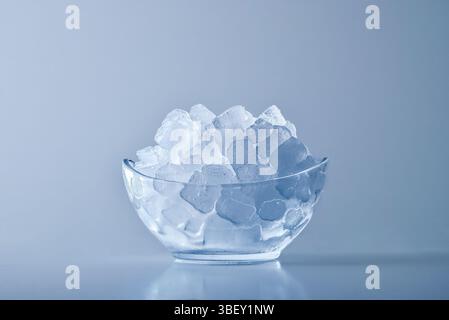 Glass bowl with a pile of ice cubes backlit on a reflective base with isolated background. Front view Stock Photo