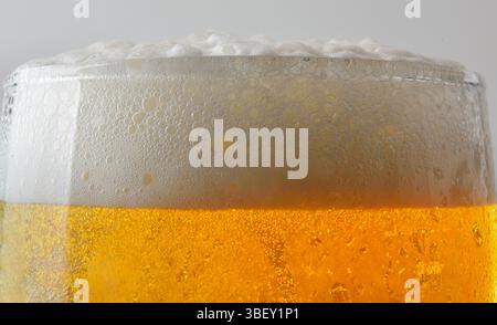 Detail of the mouth of a glass of beer filled with foam, isolated on a light background. Front view. Stock Photo