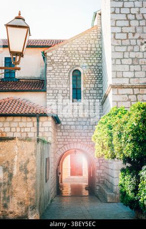 Old stone buildings with arched passage and sunlight shining through in Mediterranean town. Old town of Krk, Krk island, Croatia. Stock Photo