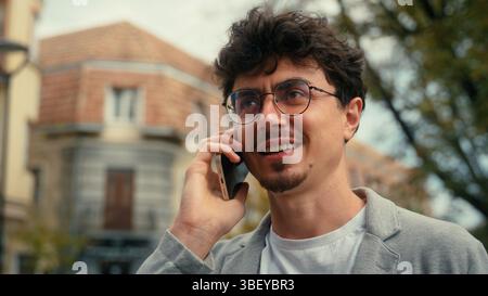 Smiling Caucasian man Hispanic guy male talking mobile phone call in city communicate with friend calling order taxi service outdoor conversation Stock Photo