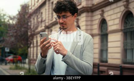 Serious concentrated Indian ethnic business man using mobile phone in city texting chatting message smartphone app internet online guy businessman Stock Photo