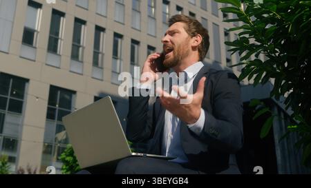 Stressed business man arguing mobile phone looking laptop throwing papers documents away in city Caucasian angry male businessman 40s employer middle Stock Photo
