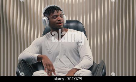 Happy young African American man guy male put on headphones listening music indoors dancing singing enjoying rhythm feeling energetic fun carefree Stock Photo