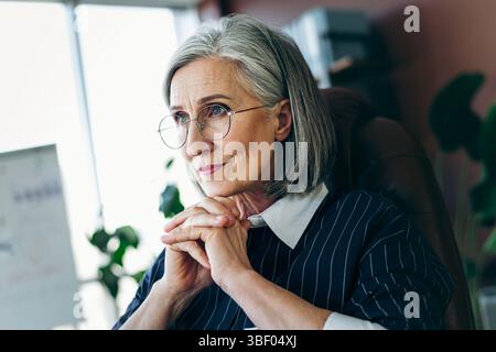 Professional mature businesswoman with grey hair working in an office workspace, focusing on her career and responsibilities Stock Photo
