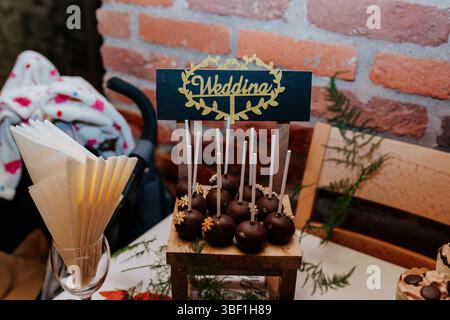 A close-up photo of a table setting with a wooden stand holding a collection of cake pops. The cake pops are dipped in chocolate and decorated with sm Stock Photo