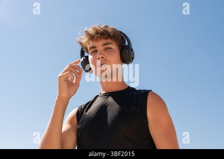 Modern Young Man Adjusting His Headphones with a Blue Sky Stock Photo