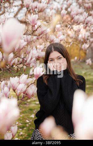 Young woman touching her face, blooming magnolia in spring Stock Photo