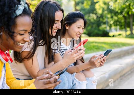 Happy students using smartphones sitting on stairs outdoors Stock Photo