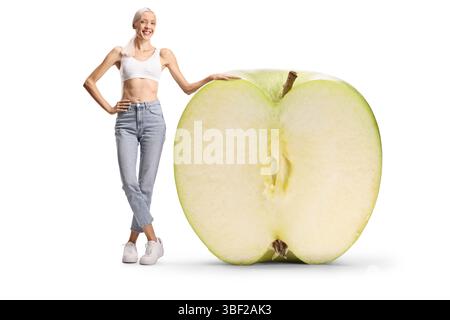 Happy slim woman standing next to a big green apple isolated on white background Stock Photo