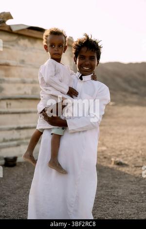 Cairo, Egypt - September 11, 2023: Two children dressed in traditional attire share a joyful moment outdoors, set against a rustic, sunlit backdrop sh Stock Photo