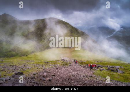 Ireland, Killarney, 11 July 2021 A group of hikers navigates rocky terrain of Carrauntoohil mountain in a misty mountainous landscape, embodying adven Stock Photo