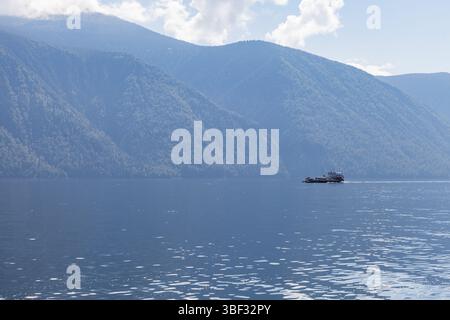 Small ferry with passenger and cars placed on deck sails the Teletskoye lake on a sunny summer day, Siberian landscape photo Stock Photo