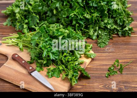 Cutting board with bunch of fresh parsley and kitchen knife on a wooden table. Selective focus. Stock Photo