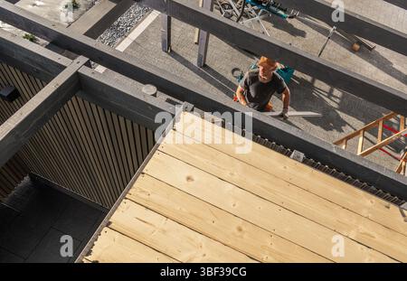 A skilled carpenter works diligently, measuring and cutting wood materials on a construction project in a bustling urban environment during daylight h Stock Photo