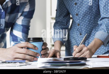 Woman writing with pen on technical drawing. Creative team of designers together working with construction blueprint. Thorough study and approval of d Stock Photo