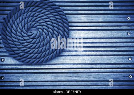 A curled mooring rope on a wooden pier. Background with Copy space. Color of the year 2020 classic blue toned Stock Photo