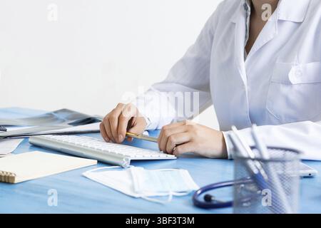 Close-up of female doctor hand with pen. Physician in medical uniform working with computer at desk. Modern technology in examination and diagnosis. P Stock Photo