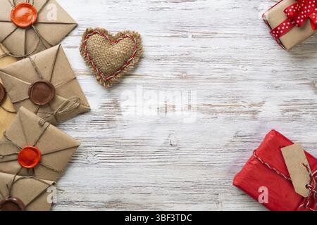 Flat lay cute composition with handmade fabric heart. Gift box and retro mail envelopes on wooden table. Happy birthday or anniversary congratulation. Stock Photo
