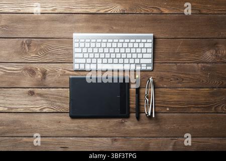 Top view office workspace composition. Flat lay vintage wooden desk with pc keyboard and graphic drawing tablet. Design and creativity. Time managemen Stock Photo