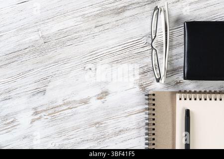 Still life of modern office workspace with supplies. Spiral notepad and black leather wallet on white wooden surface. Time management and day planning Stock Photo