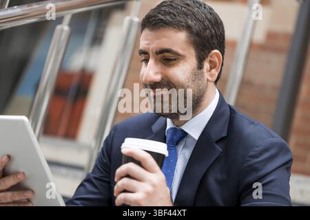Confident businessman sitting on steps with tablet and coffee Stock Photo