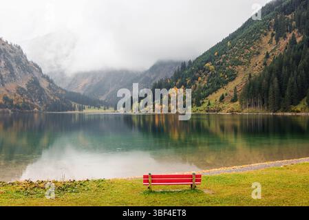 Red bench on the bank of alpine lake on cloudy autumn day. Bench with a view of Vilsalpsee lake in Tyrol, Austria. Stock Photo
