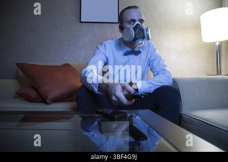 Handsome young caucasian man in a blue shirt and respirator watching TV Stock Photo
