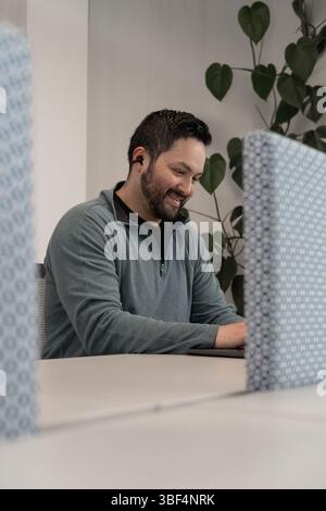 A tech-savvy young man concentrates on his laptop, developing software in a lively coworking hub filled with startup energy. Stock Photo