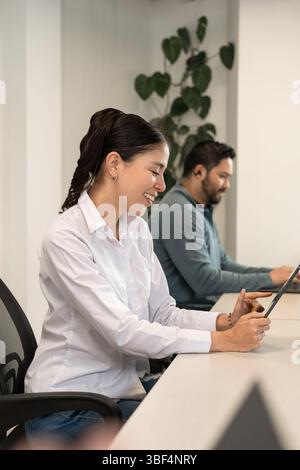 Modern startup energy: a man and woman smile as they exchange ideas and work side by side on laptops in a bright creative workspace. Stock Photo