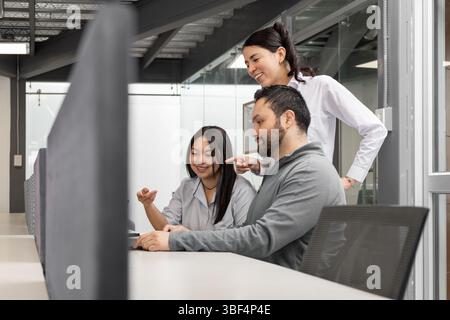 Coworkers focus on the screen while analyzing the latest sales report, collaborating in a modern, open office environment. Stock Photo