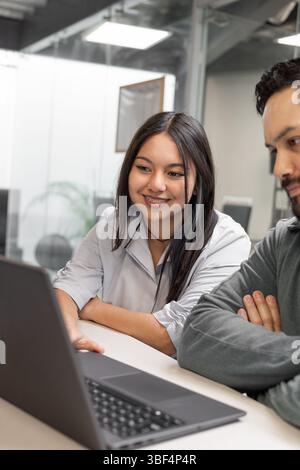 Two colleagues share a focused moment in front of the laptop, collaborating in a relaxed and modern office space. Stock Photo