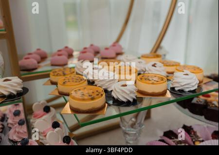 A beautifully arranged dessert table features various mini cheesecakes, delicate pink macarons, and other sweet pastries presented on tiered glass sta Stock Photo