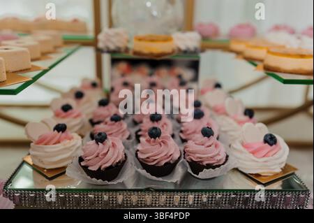 A luxurious spread of pink-frosted cupcakes decorated with blueberries and assorted mini pastries arranged on sparkling golden tiered stands ideal for Stock Photo